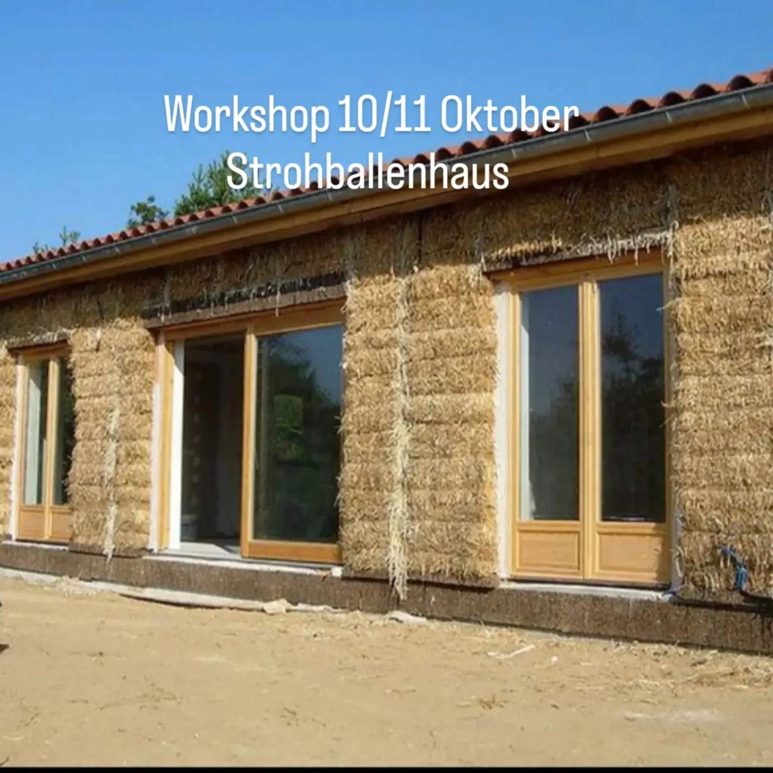 Strohballenhaus im Rohbau mit Strohballen und Holzfenstern während des Workshops